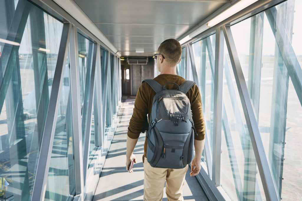 Man walking down glass hallway in airport while wearing a backpack